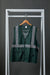 Front view image of a green polyester safety vest with zipper closure, silver reflective tape and front pockets. The green safety vest is hanging on a wooden hanger from white metal display bar