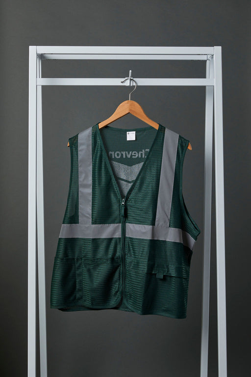 Front view image of a green polyester safety vest with zipper closure, silver reflective tape and front pockets. The green safety vest is hanging on a wooden hanger from white metal display bar