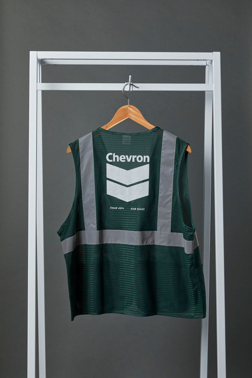 Back view image of a green polyester safety vest with silver reflective tape and the Chevron logo printed on it in white. The green safety vest is hanging on a wooden hanger from white metal display bar